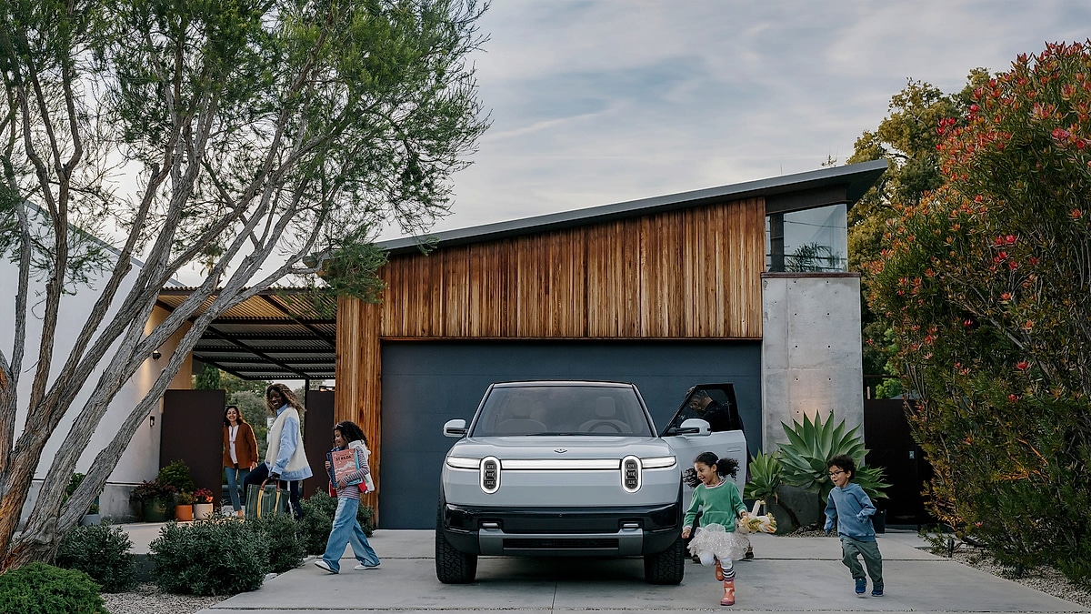 White Rivian R2 electric SUV parked in residential driveway with family and children around a modern mid-century home