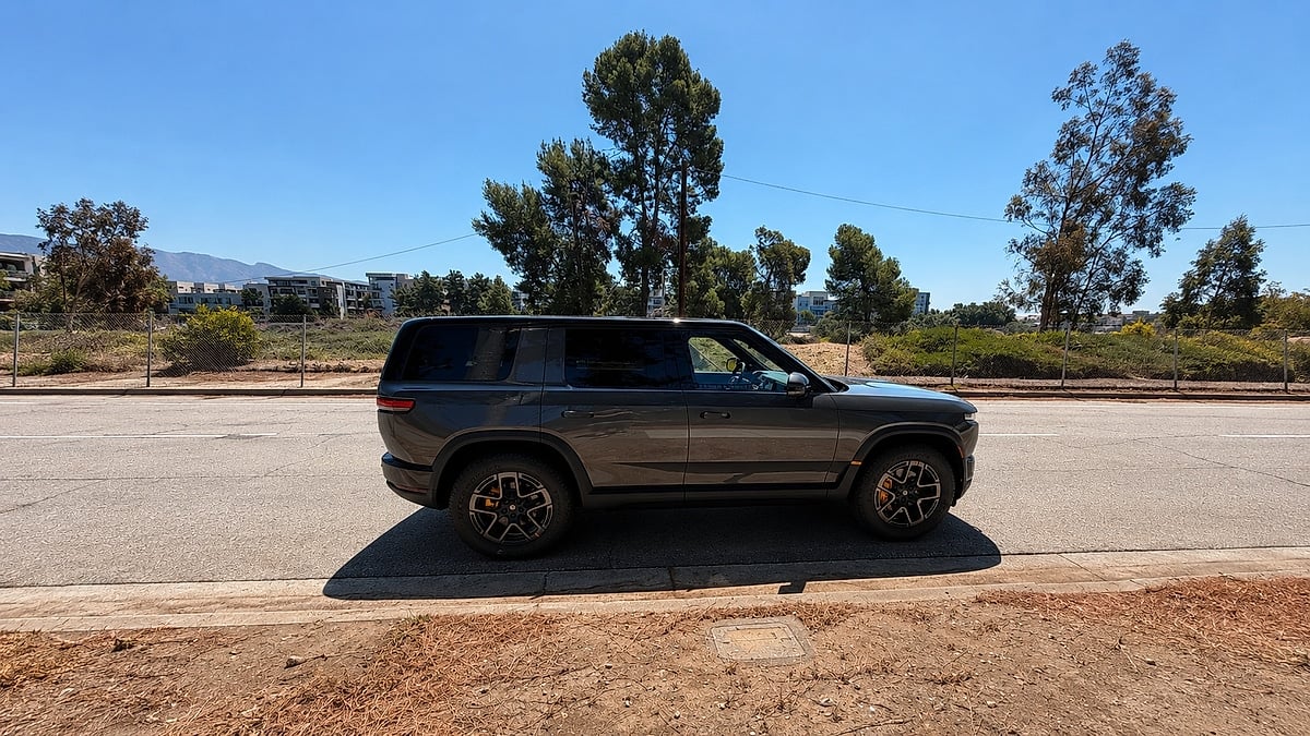 Gray Rivian R2 parked in side profile on a sunny city street.