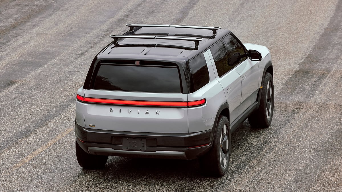 Overhead rear three-quarter view of the 2027 Rivian R2 electric SUV showing the full-width red taillight bar, roof rack, and Rivian badging
