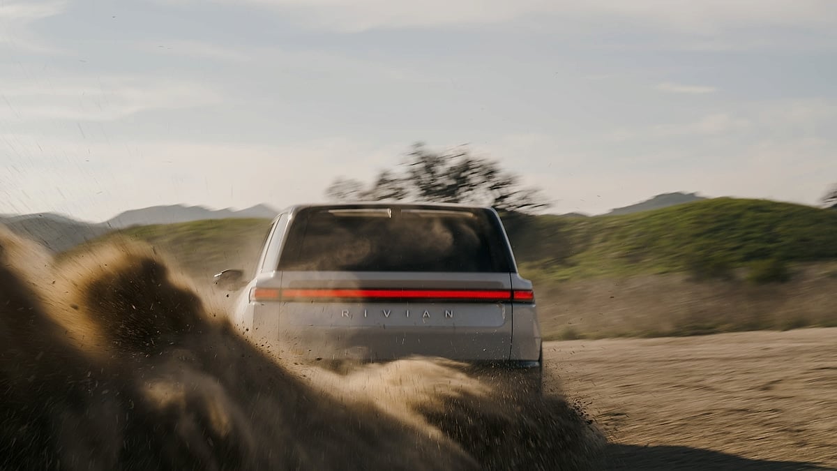 Rear view of a Rivian R2 driving through dirt and kicking up dust on an off-road trail.
