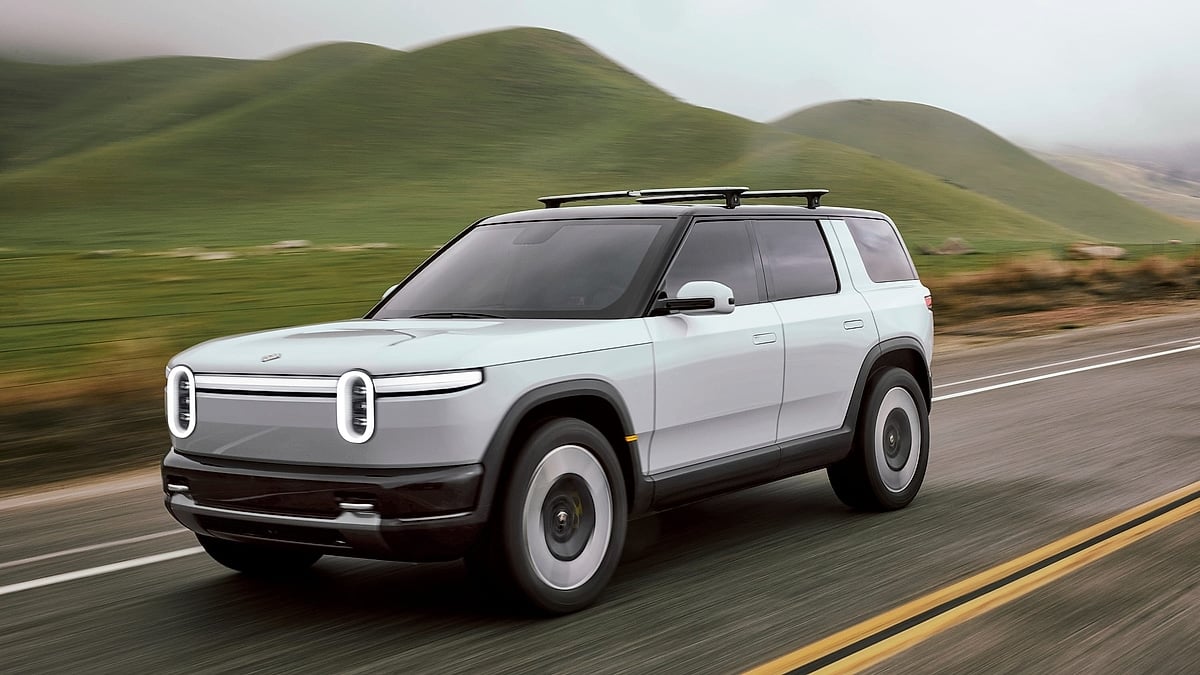 Rivian R2S electric SUV driving along a winding road through green hills