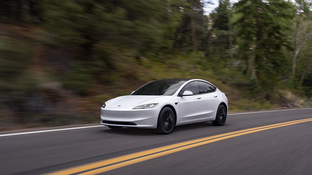 White Tesla Model 3 driving on road surrounded by trees