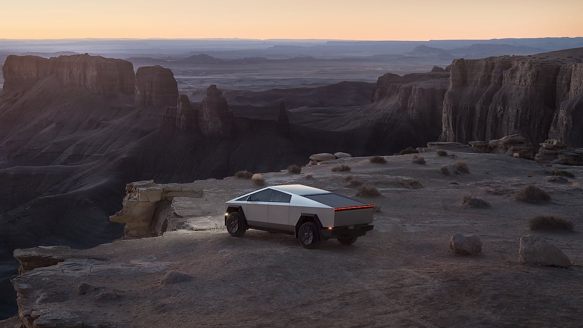 Tesla Cybertruck parked near a canyon overlook at sunset with cliffs and desert formations in the background.