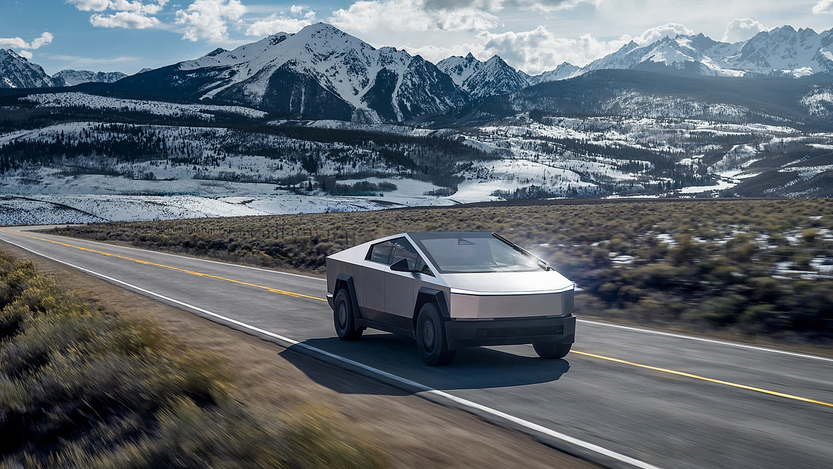 Tesla Cybertruck driving on a highway with snow-covered mountains in the background.