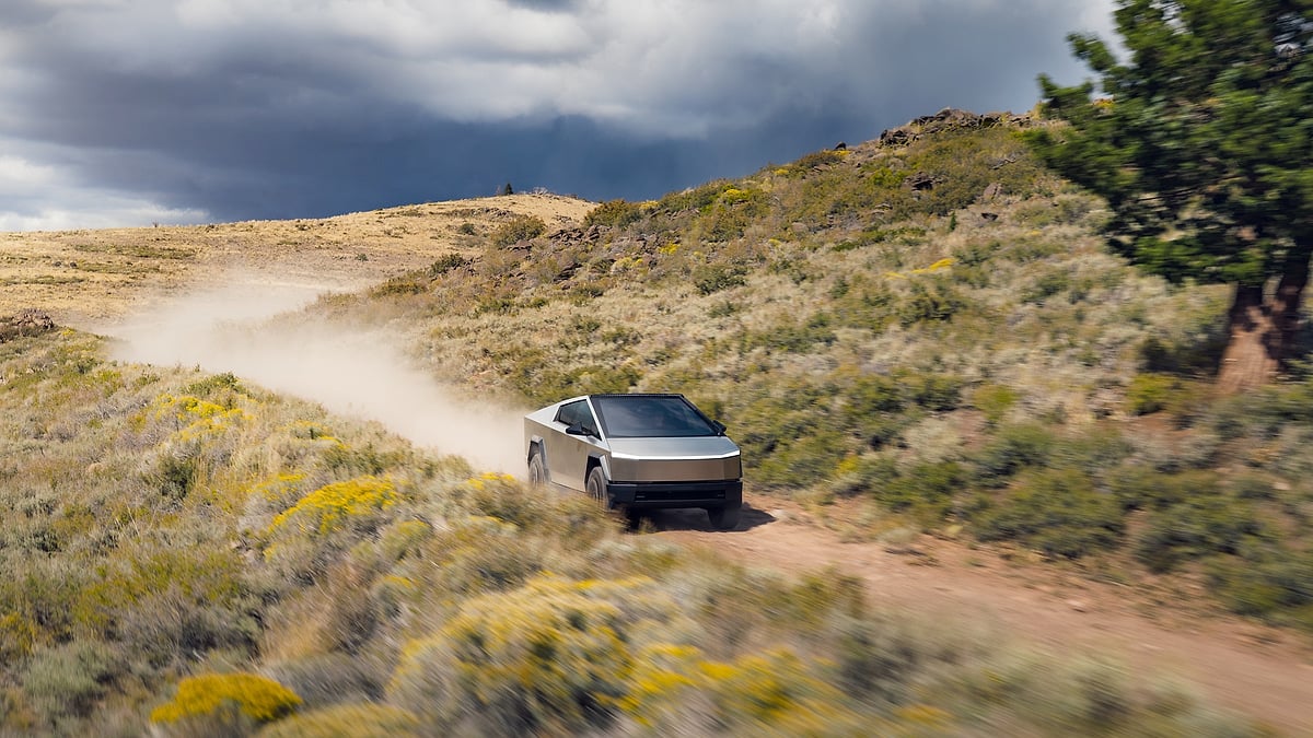 Tesla Cybertruck driving off-road on a dusty trail under dark storm clouds.