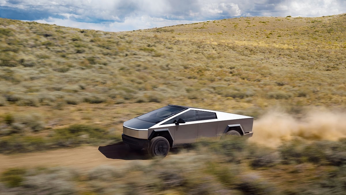 Tesla Cybertruck driving off-road through desert terrain and leaving a dust trail behind it.