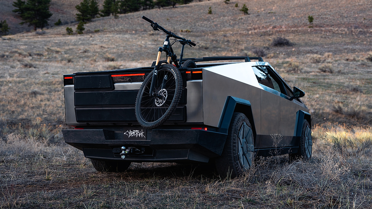 Rear three-quarter view of a Tesla Cybertruck parked off-road with a mountain bike mounted on the back.