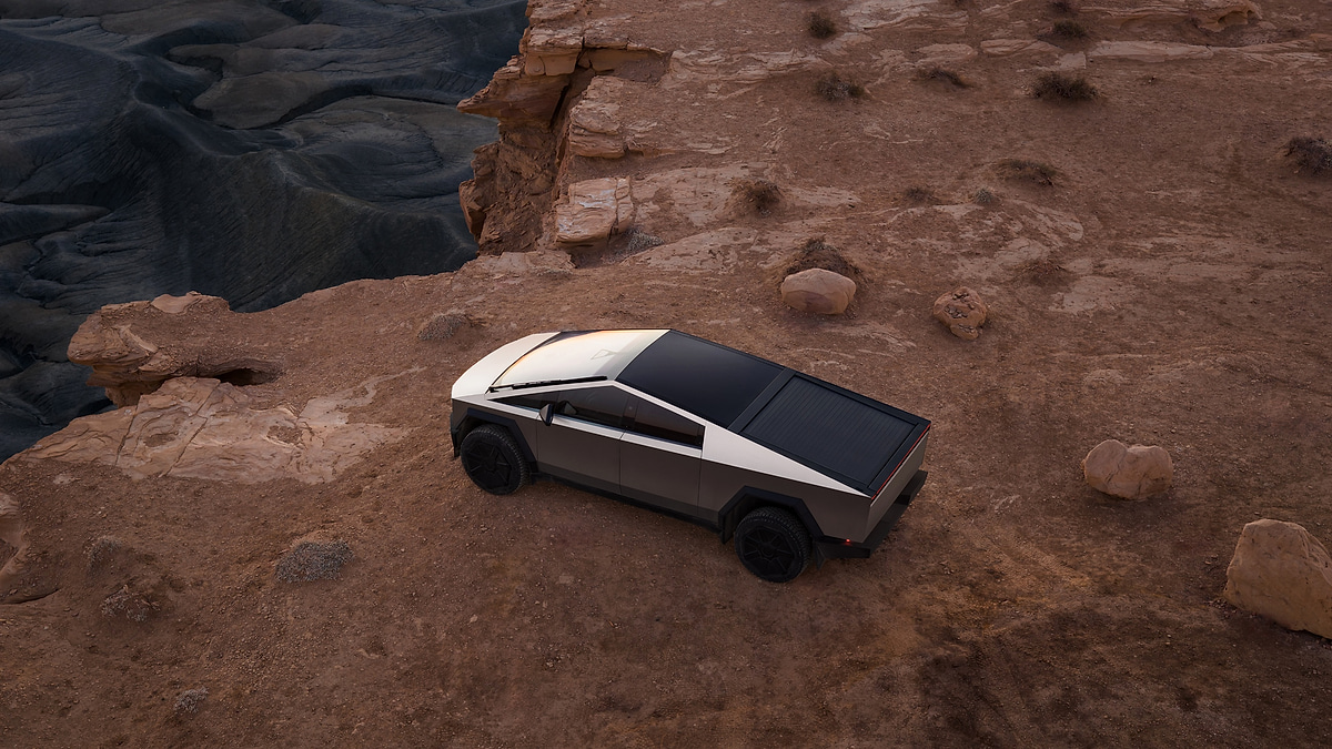 Tesla Cybertruck shown in side profile on a rocky ledge against a darkening sky.