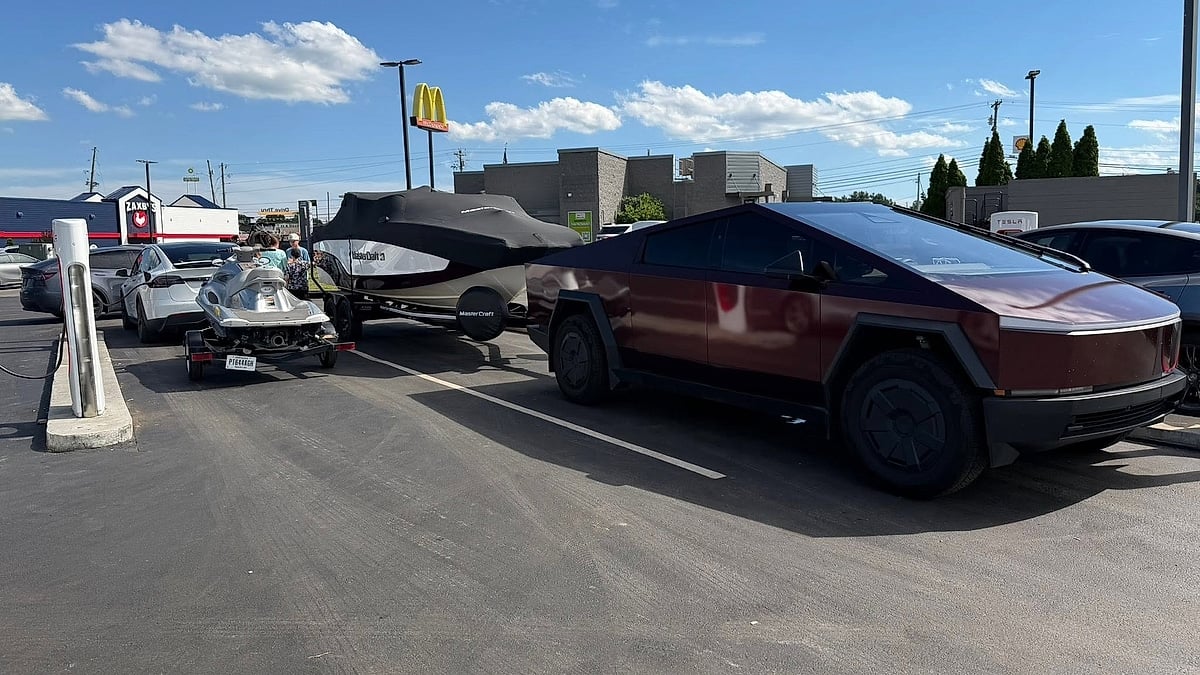 Tesla Cybertruck towing a MasterCraft boat at a Tesla Supercharger station with a white Tesla Model Y nearby.