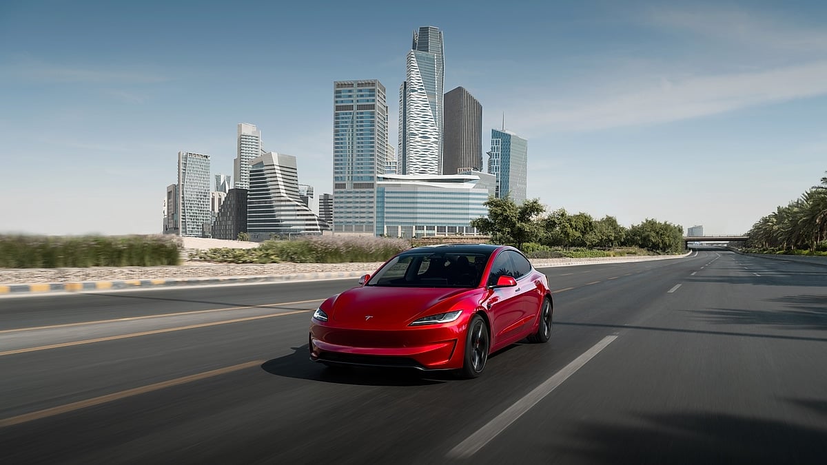 Red Tesla Model 3 Performance driving on a city highway with modern buildings in the background.