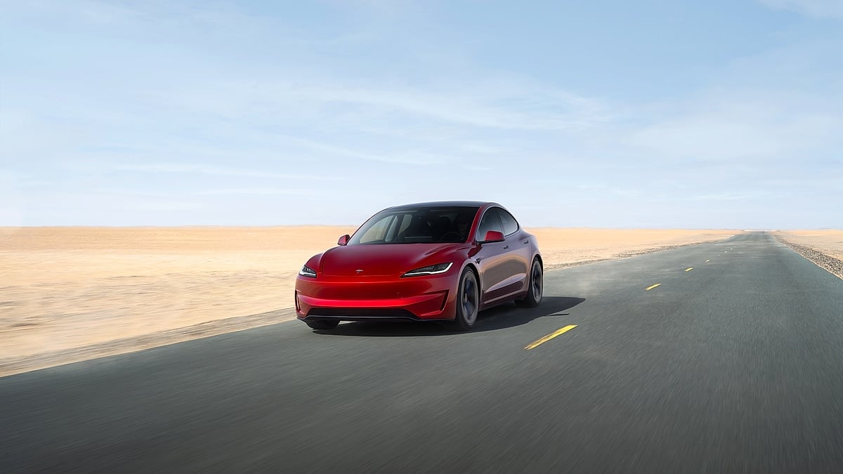 Red Tesla Model 3 Performance driving on an open desert highway in a front three-quarter view.