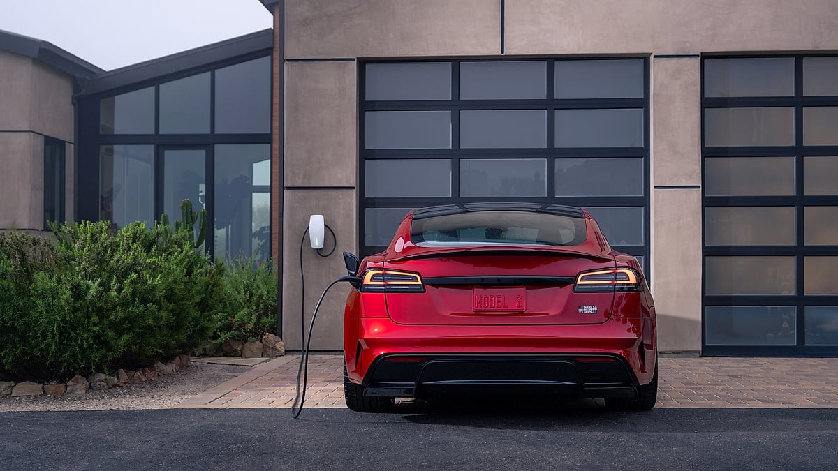 Rear view of a red Tesla Model S charging in front of a modern home garage.
