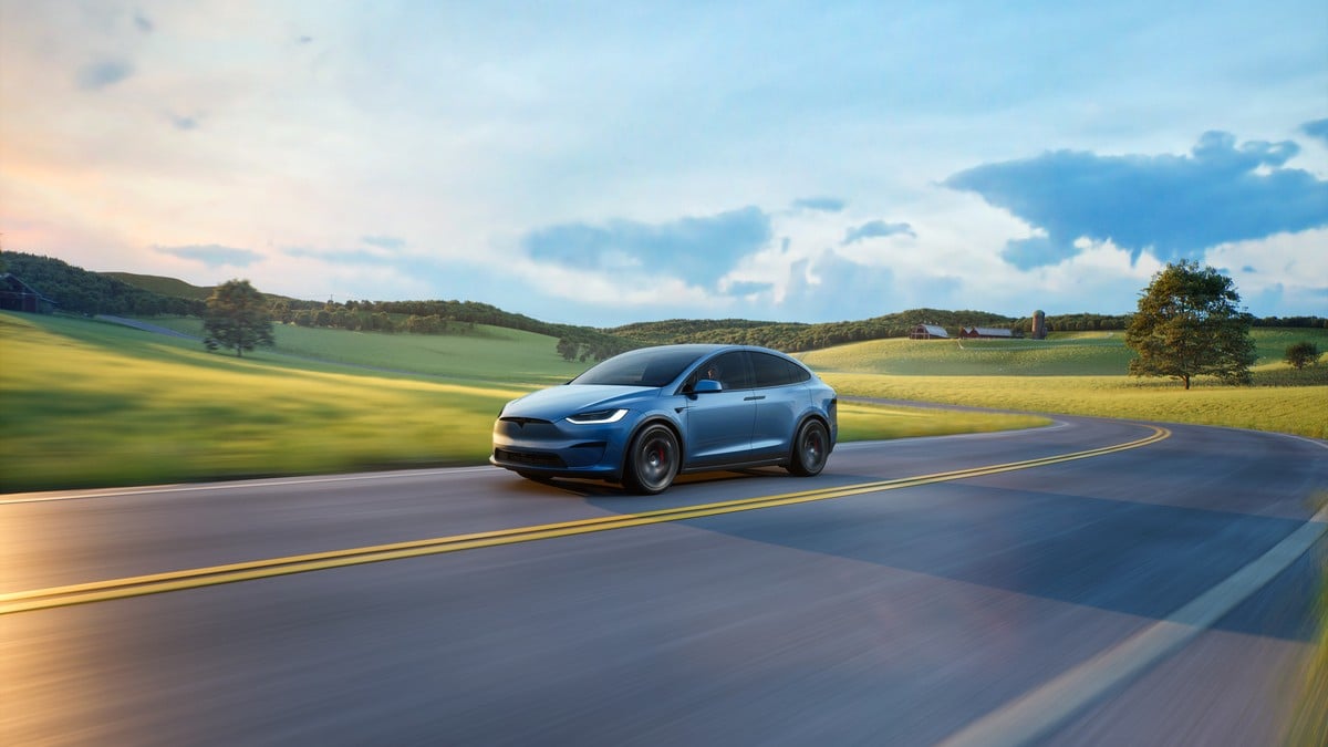 Blue Tesla Model X electric SUV captured from a front three-quarter angle driving through rolling countryside.