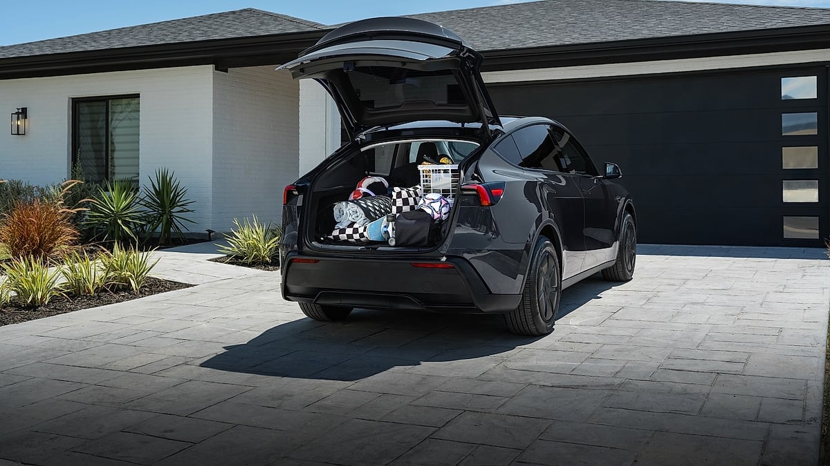 Tesla Model Y parked in a driveway with the rear hatch open, showing luggage and cargo space.