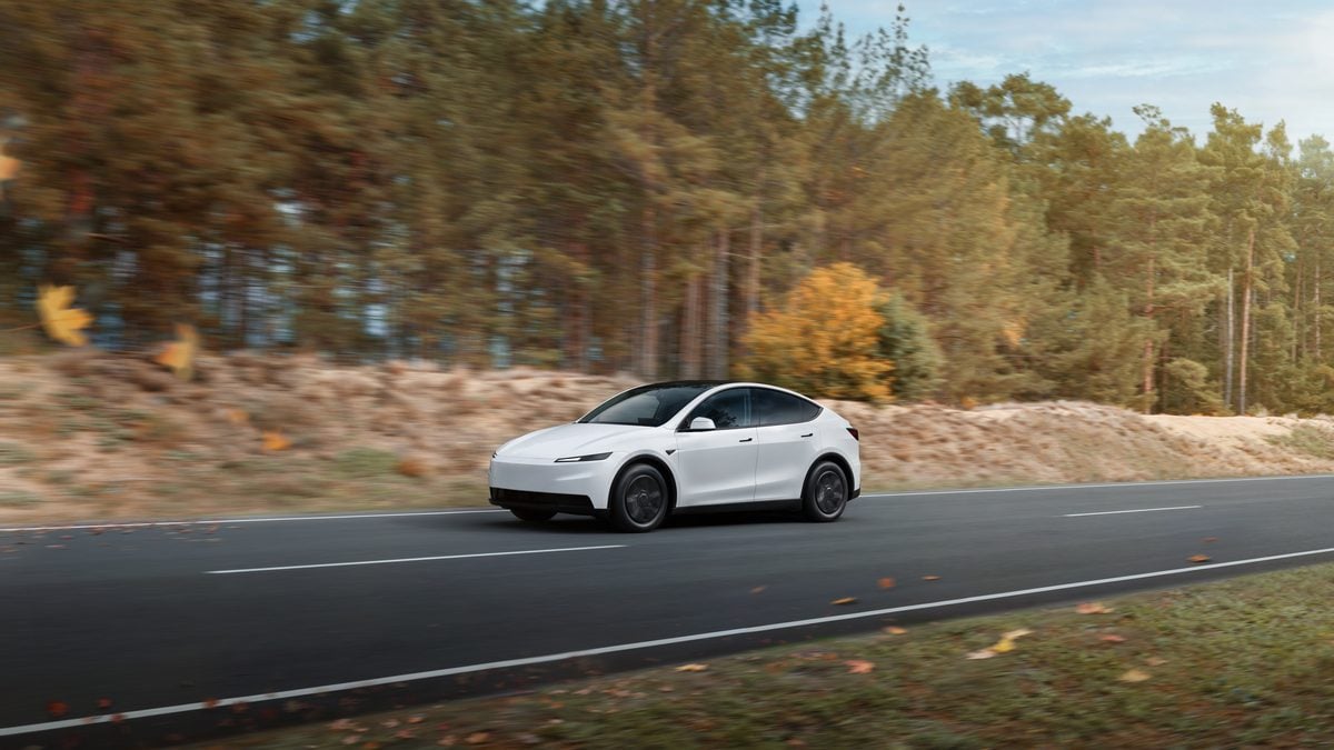 White Tesla Model Y electric SUV driving on a desert road, front three-quarter angle with aerodynamic design and minimalist styling.