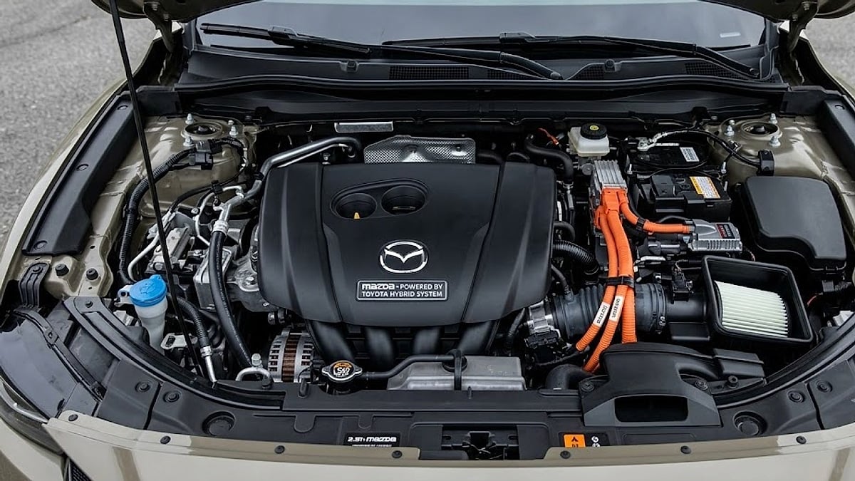 The open engine bay of a Mazda CX-50 Hybrid showing bright orange high-voltage cables and a shared Toyota powertrain