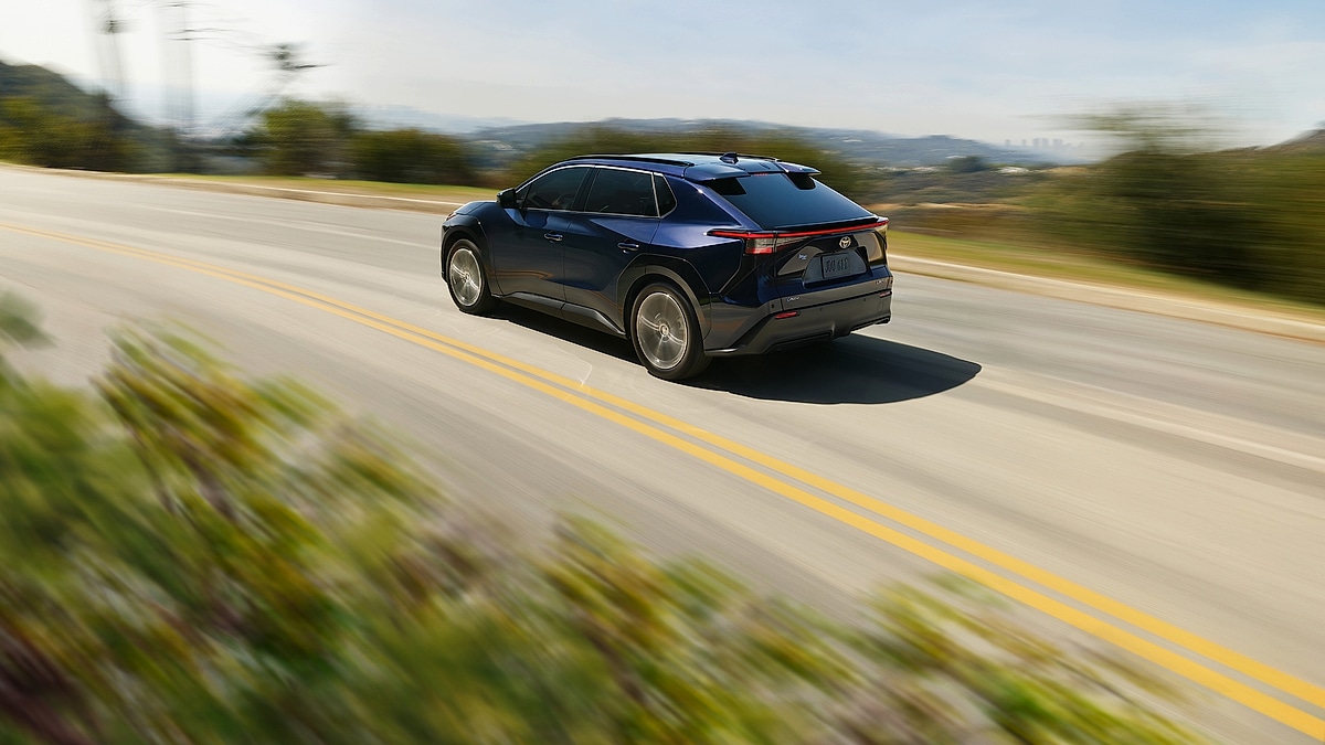 Blue Toyota bZ4X electric SUV driving on an open highway with blurred landscape