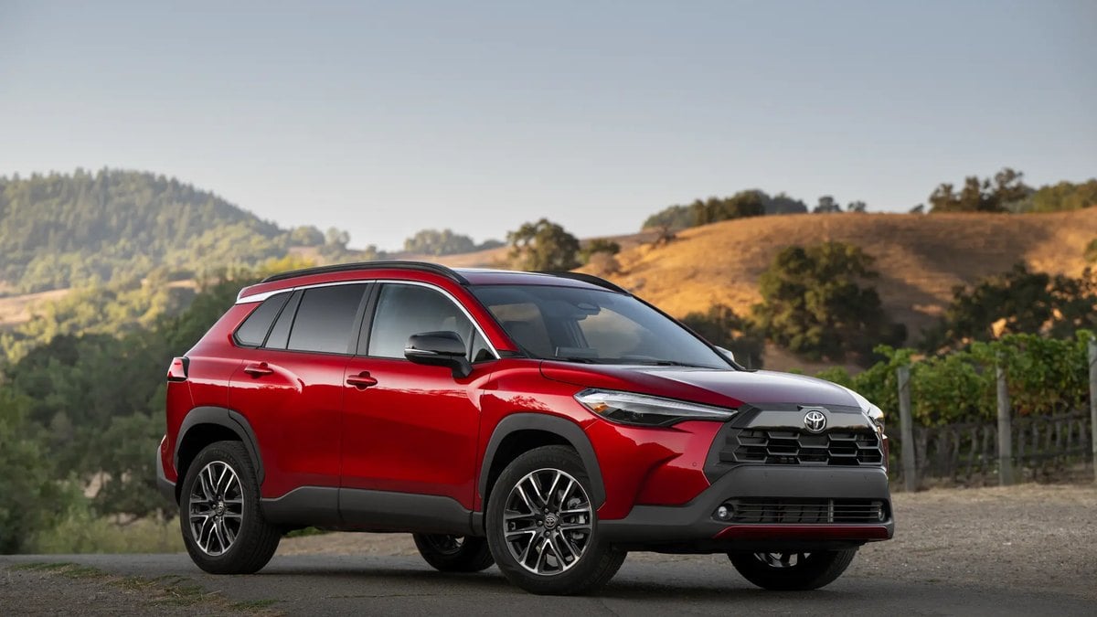 Toyota Corolla Cross in Soul Red Crystal parked on mountain overlook with scenic landscape vista, showcasing side profile and modern SUV design