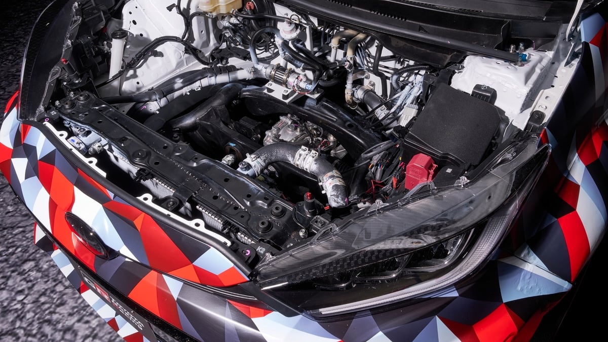 Close-up of the open engine bay on a camouflage-wrapped Toyota GR prototype vehicle, showing wiring and engine components