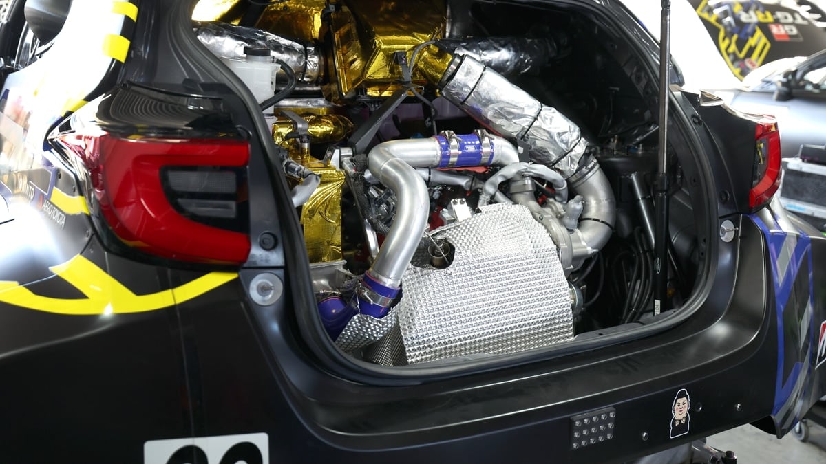 Close-up of a Toyota GR race car's rear-mounted engine bay, showing turbocharger, exhaust piping, and gold heat shielding