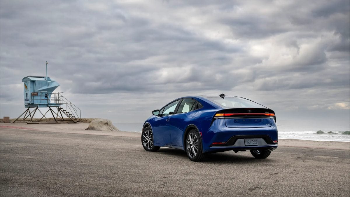 Rear three-quarter view of a blue Toyota Prius parked near a beach lifeguard tower, highlighting taillight design and hybrid badge.