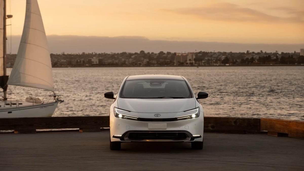 Front view of a white Toyota Prius parked by a marina at dusk, showcasing LED headlights and aerodynamic styling.