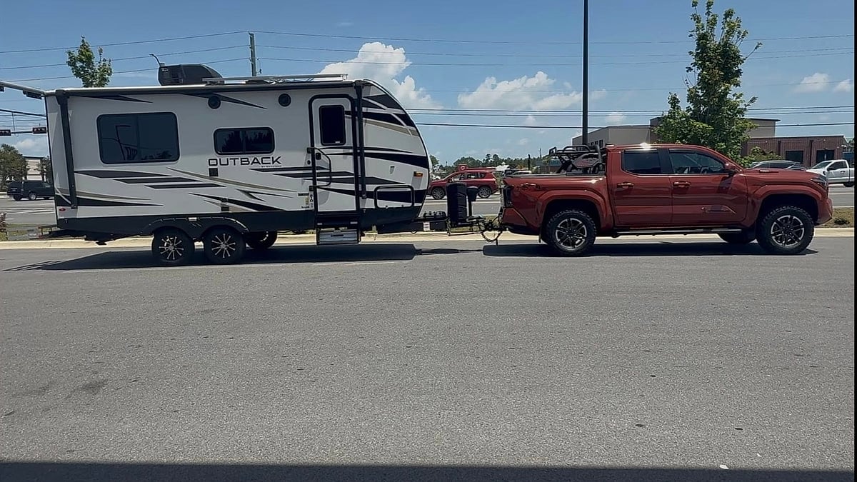 Toyota Tacoma towing an Outback travel trailer in a side-profile view on a sunny street.