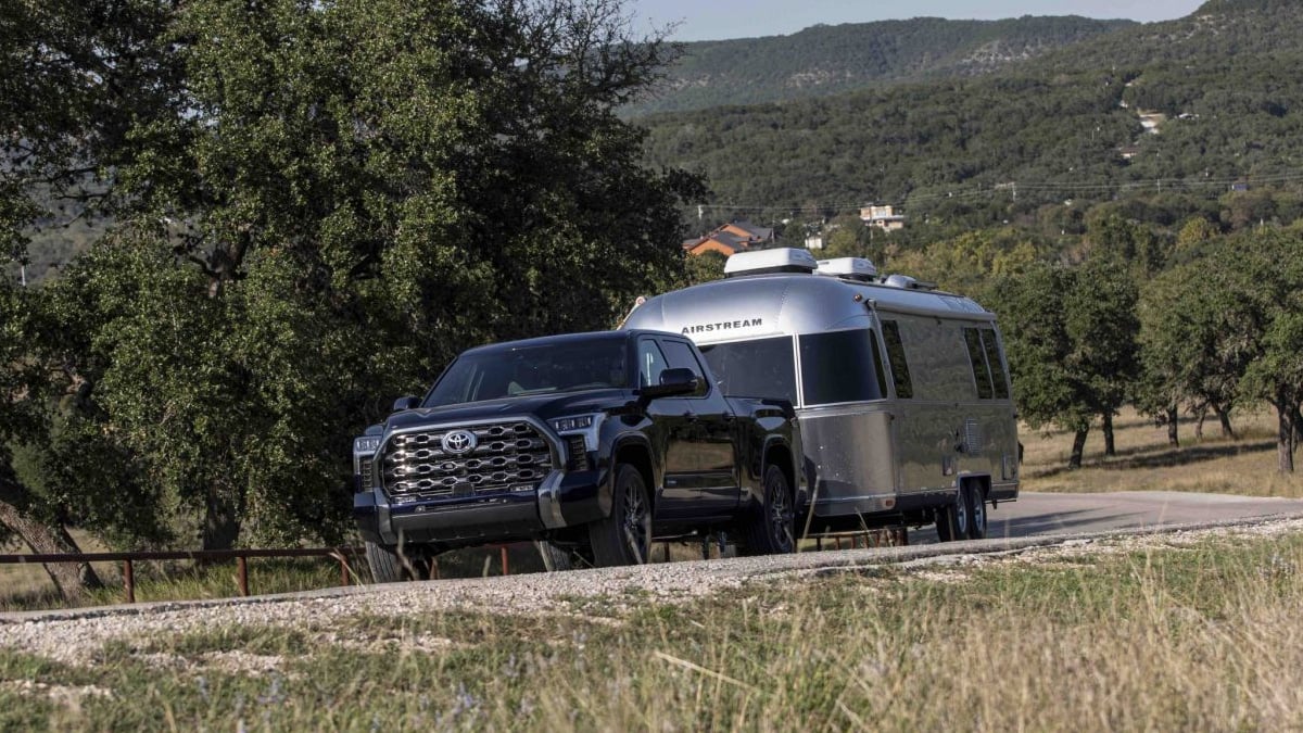 Dark blue Toyota Tundra Platinum towing a silver Airstream trailer on a rural road through rolling hill country