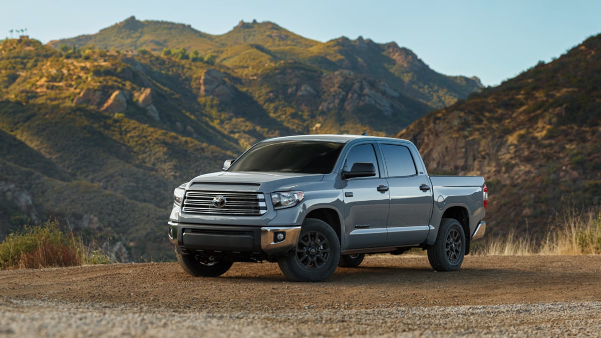 Silver Toyota Tundra pickup truck parked on a gravel overlook with rugged mountains in the background, front three-quarter view