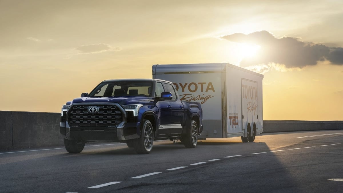 Dark blue Toyota Tundra towing a Toyota Racing enclosed trailer on a road at sunset