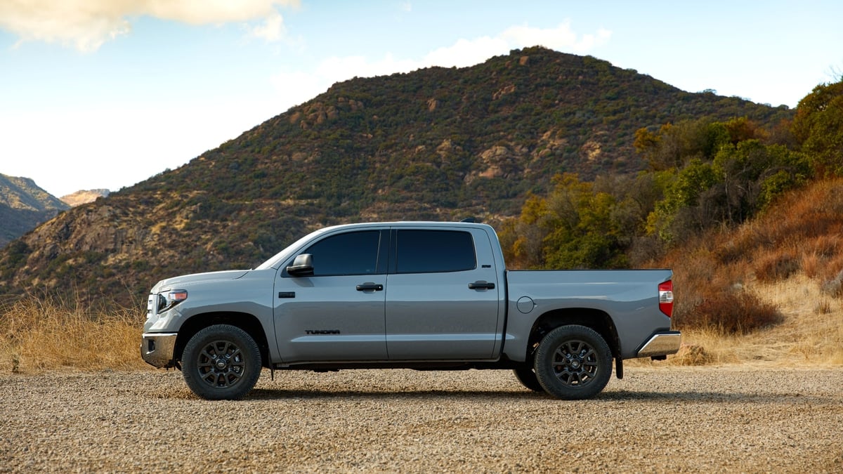 Silver Toyota Tundra Trail Edition pickup truck parked on a gravel lot with mountains in the background, side profile view