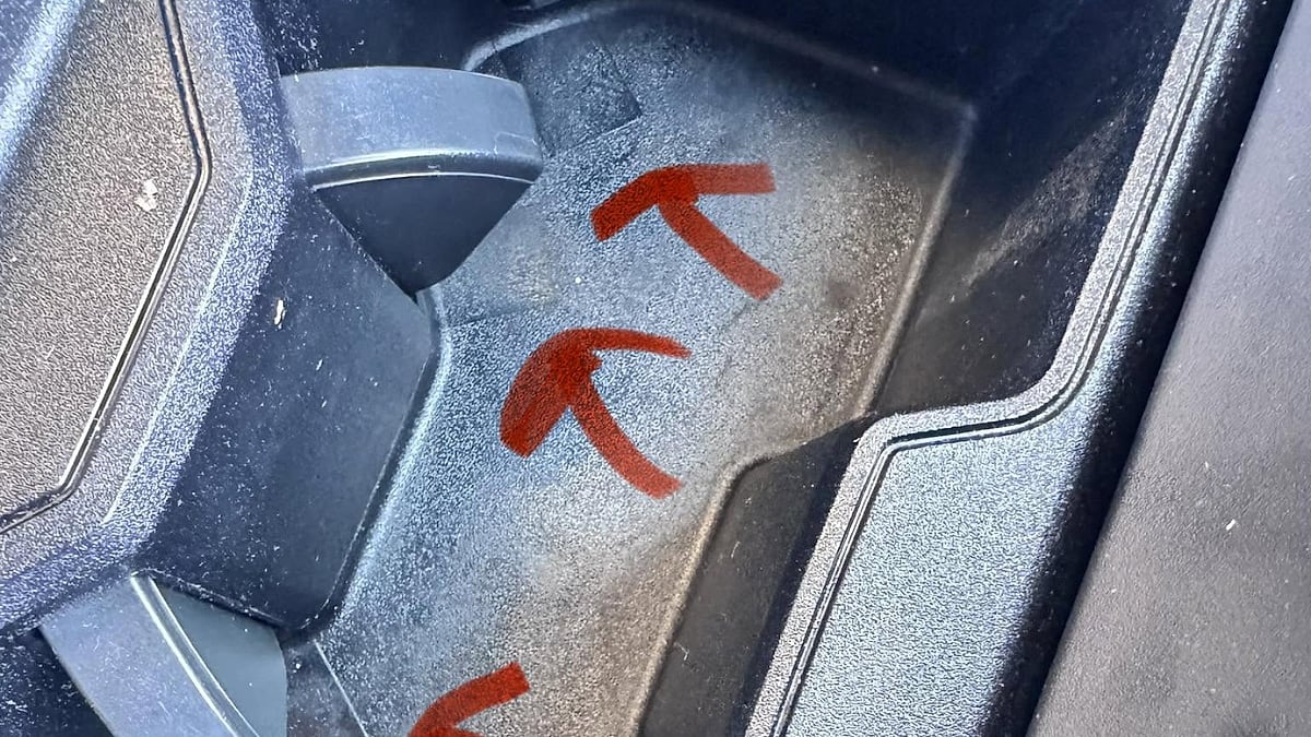 Close-up of the cupholder area inside Vu J Nguyen's Toyota Tundra, with red arrows highlighting openings beneath the cupholder where spilled liquid may have traveled into the center console.