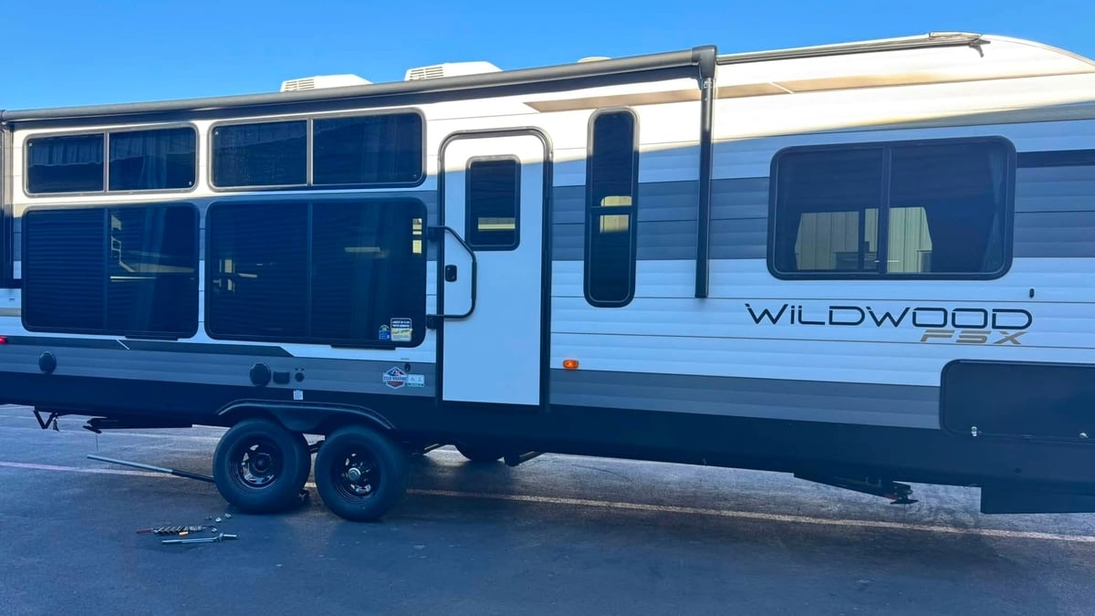 Side view of a white and gray Wildwood FSX travel trailer parked in a lot, with tools laid out near the wheels