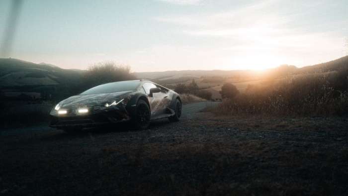 A Lamborghini Huracan Sterrato is pictured parked at the side of a gravel road as the sun sets over hills in the background.