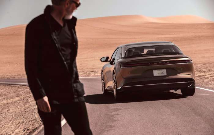 A gold Lucid Air is seen parked on a road running through a desert.