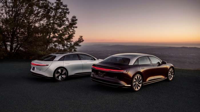 A Lucid Air Grand Touring and Grand Touring Performance are pictured parked on a hill at sunset.