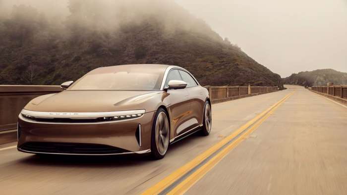 Front three-quarter image of a gold Lucid Air Dream Edition driving through some misty mountains.