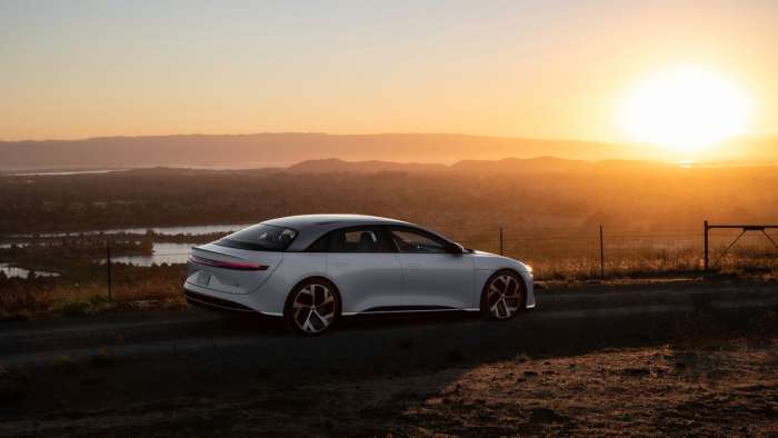 A white Lucid Air is pictured parked on a hill bathed in golden light from a sunset.
