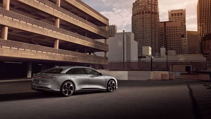 Rear three-quarter view of a silver Lucid Air Touring parked with a cityscape in the background.