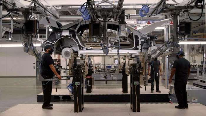 Image showing a mid-production Lucid Air raised up on a crane at the battery installation area of the assembly line.