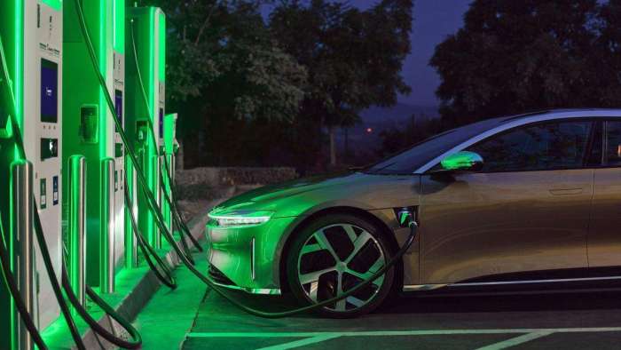 A gold Lucid Air Dream Edition is pictured parked at an Electrify America charger bathed in green light.