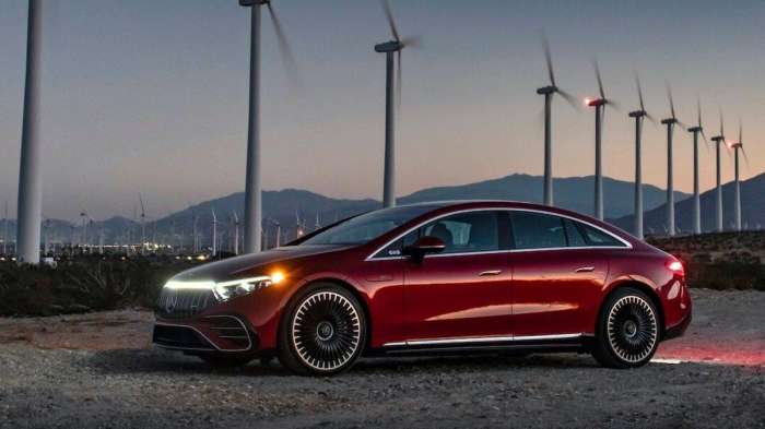 Image of a red Mercedes EQS parked in front of some wind turbines.