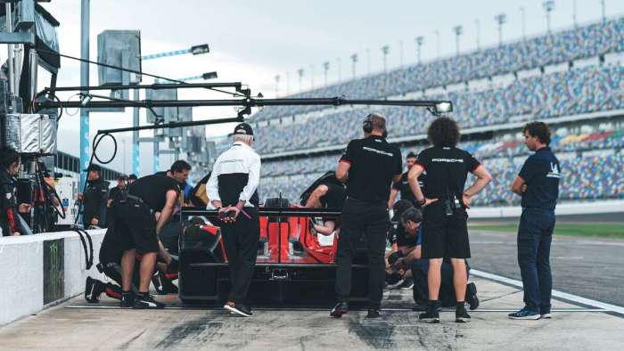 Image of the rear of the Porsche 963 as it sits in the Daytona pits surrounded by crew and team boss Roger Penske.