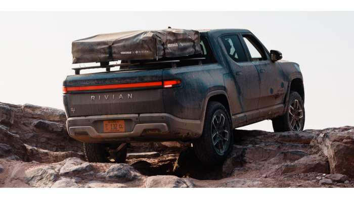 Image showing a dark blue Rivian R1T clambering over some rocks with a rooftop tent attached on top of the bed.