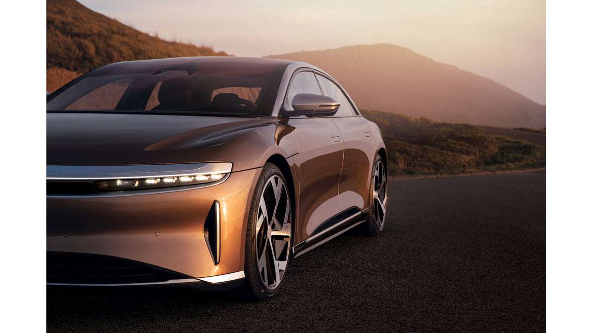 A gold Lucid Air is seen close-up parked in front of some mountains.