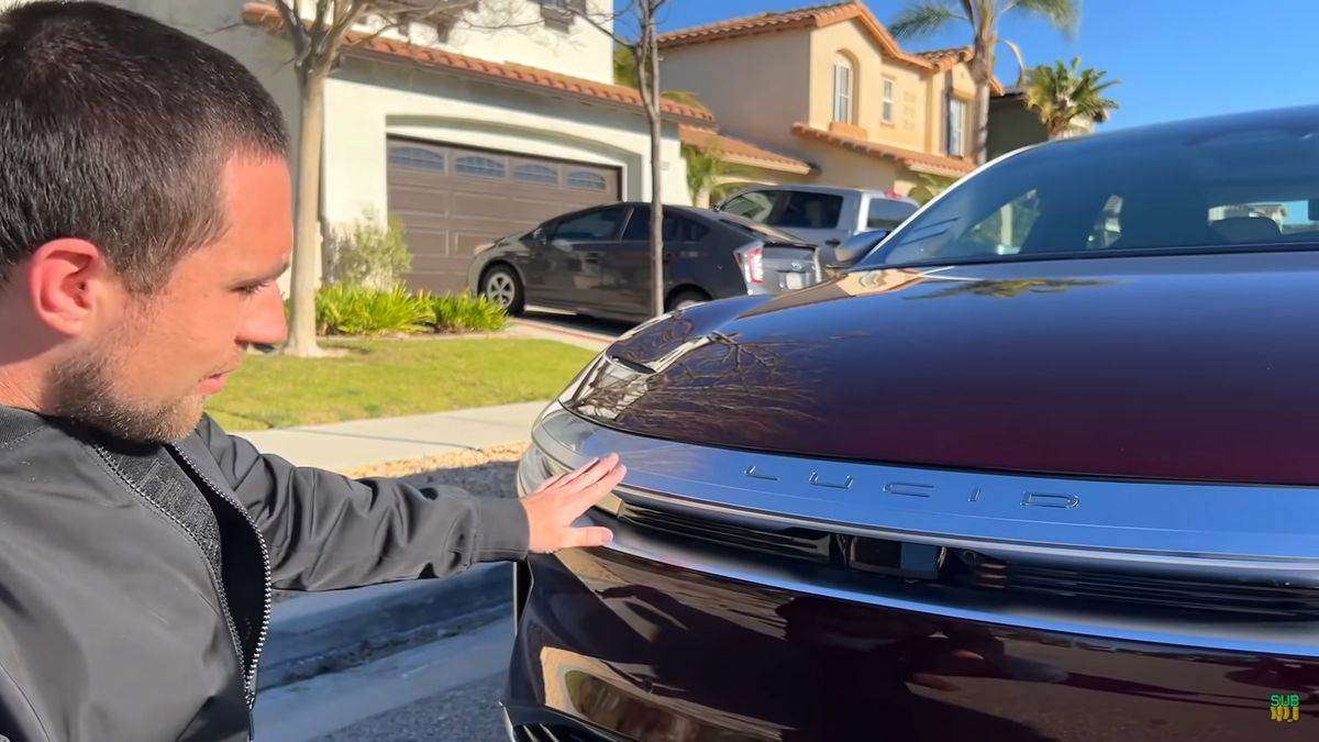 Image showing Kevin from the Meet Kevin YouTube channel crouching by the front of his Zenith red Lucid Air Dream Edition.