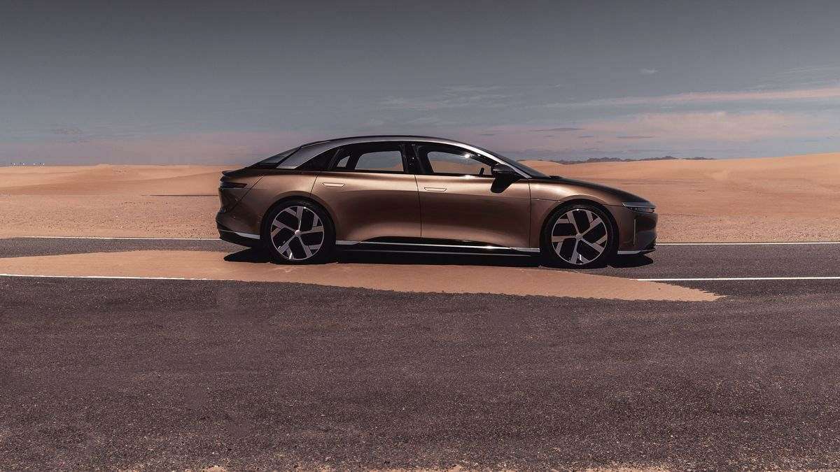 Image of a Eureka Gold Lucid Air Dream Edition in the desert of Saudi Arabia with sand blowing across the road.