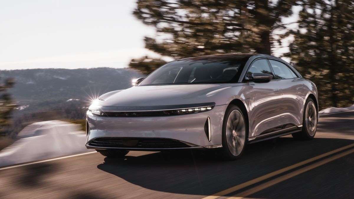 Image of a white Lucid Air driving in the sunshine on a mountain road.