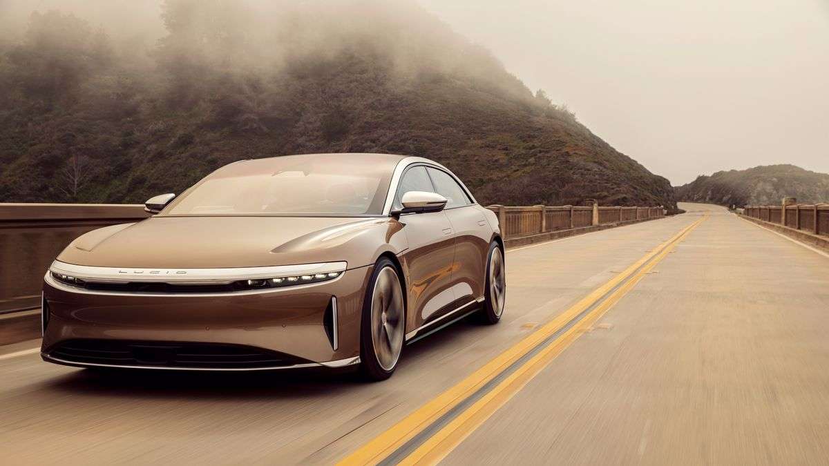 Image showing a Eureka Gold Lucid Air driving on a bridge with cloudy mountains in the background.