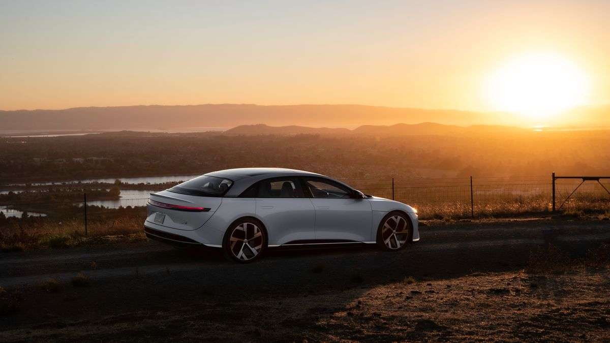 A white Lucid Air Grand Touring is parked on a hilltop at sunset.